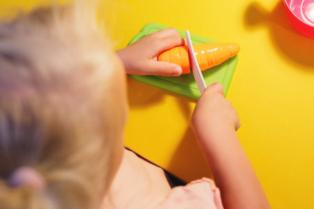 A child cuts a toy carrot on a yellow background with a toy knifeの写真素材