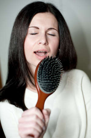 Young tousle-headed brunette pretending to sing with her hair brush as a microphoneの写真素材