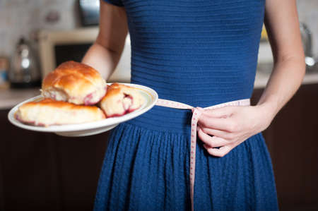 young woman holds pie and a measuring tape, care about health