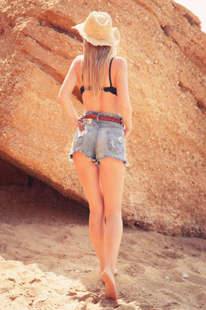 Beautiful young woman in straw hat and jeans shorts on the beach の写真素材