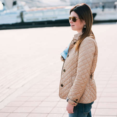 Outdoor lifestyle portrait of woman walking at coast. Fashion style. young woman dressed in branded clothes enjoys warm, spring weather. の写真素材