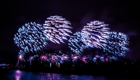 Abstract, blurry, bokeh-style colorful photo of fireworks in a purple tone above the riverの写真素材