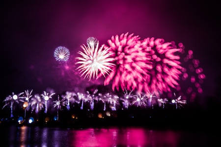 Abstract, blurry, bokeh-style colorful photo of fireworks in a purple tone above the riverの写真素材