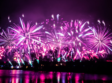 Abstract, blurry, bokeh-style colorful photo of fireworks in a purple tone above the riverの写真素材