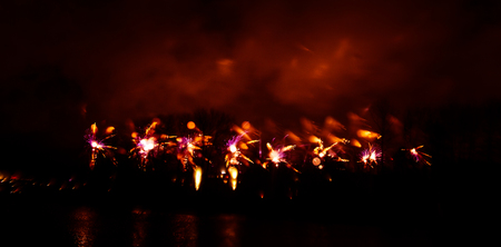 Abstract, blurry, bokeh-style colorful photo of fireworks in a red tone above the river