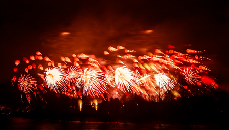 Abstract, blurry, bokeh-style colorful photo of fireworks in a red tone above the riverの写真素材