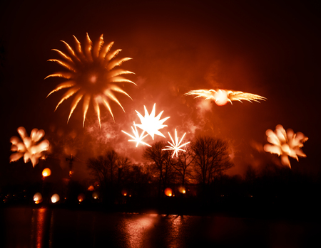 Abstract, blurry, bokeh-style colorful photo of fireworks in a red tone above the river
