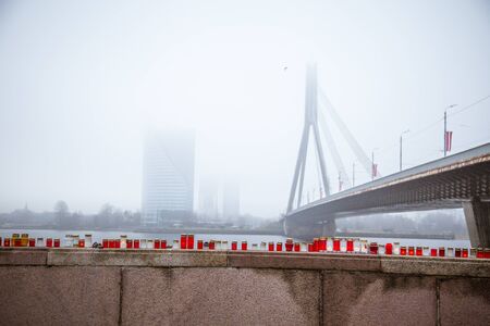 A beautiful red and white candles on the railing of a river side in the foggy november morning in Rigaの写真素材