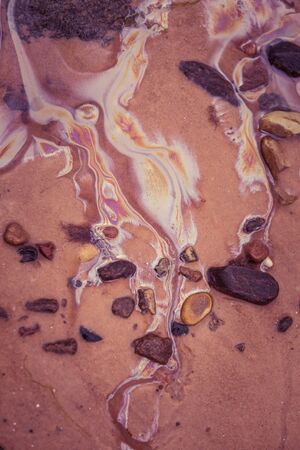 Colorful patterns of oil in the beach sand. Pollution patterns on the shore of Baltic sea. Colorful,...