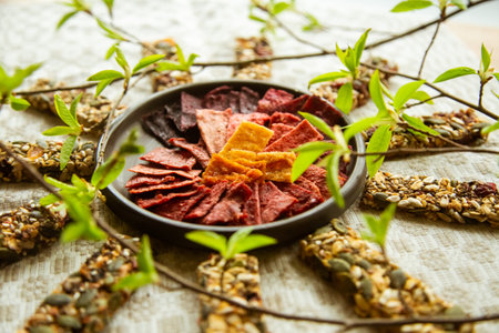 A circular composition on the table with homemade fruit leather pieces in the bowl and granola bars of seeds and nuts around ir. Fresh, green spring sprouts in the vase. Tasty, vegan, organic, homemade snacks for christmas, spring, hiking.の写真素材