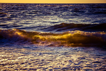 A beautiful sunset scenery with breaking waves close to the sandy shore. Sun shines in on the water...