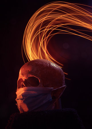 An artistic studio shot of artificial skull with face mask and colorful light streaks in background....
