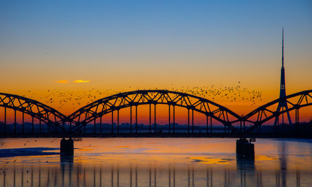 A beautiful sunrise scenery with iron bridge over the frozen river Daugava in Latvian capital city Riga. Winter landscape of Northern Europe.の写真素材