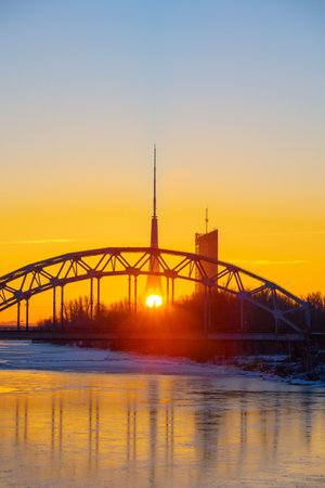 A beautiful sunrise scenery with iron bridge over the frozen river Daugava in Latvian capital city Riga. Winter landscape of Northern Europe.の写真素材