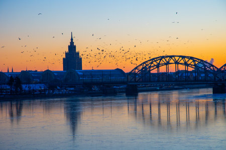A beautiful sunrise scenery with iron bridge over the frozen river Daugava in Latvian capital city Riga. Winter landscape of Northern Europe.の写真素材