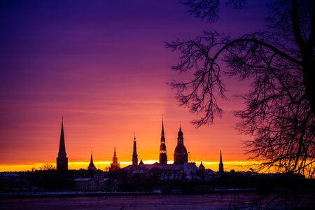 A beautiful, colorful sunrise landscape with city centre building silhouette against bright morning sky. A winter lansdcape with frozen river Daugava in Latvia capital Riga.の写真素材