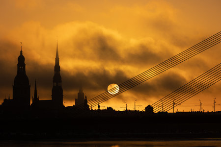 A beautiful Riga cityscape with suspension bridge over the riwer during colorful sunrise. Buildings against colorful sky. Norther Europe morning with warm sky.の写真素材