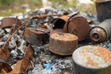Old, rusted metal cans in burned ash. Trash in abandoned army base, burned, rusty.の写真素材