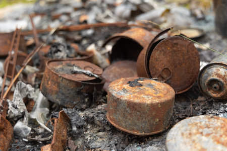 Old, rusted metal cans in burned ash. Trash in abandoned army base, burned, rusty.の写真素材