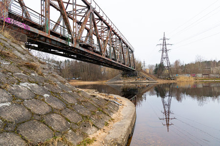 A metal truss bridge over the river in overcast spring day. Natural springtime scenery in Riga,...