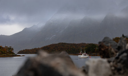 A small white fishing ship in the fjord in Lofoten islands, Norway. Overcast autumn day with mountains. Seasonal scenery of Scandinavia.の写真素材
