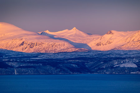 A beautiful snowy mountains over the fjord in arctic golden hour in Norway arctic. Arctic nature in...