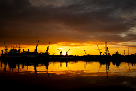 Beautiful metal crane silhouettes against the setting sun disc in harbour. Industrial cityscape of Riga, Latvia.の写真素材