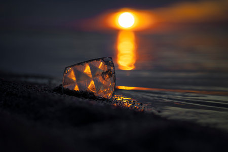 A beautiful faceted glass shard reflecting sunset sun at the Baltic Sea beach. Artistic evening scenery in Latvia, Europe.の写真素材