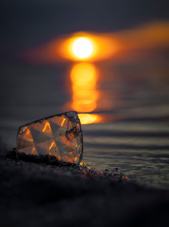 A beautiful faceted glass shard reflecting sunset sun at the Baltic Sea beach. Artistic evening...