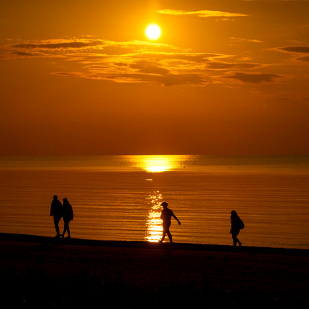 A beautiful summer sunset scenery with people silhouettes walking on a beach, enjoying Baltic Sea costline. Evening landscape of Latvia, Europe.の写真素材