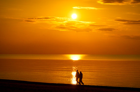 A beautiful summer sunset scenery with people silhouettes walking on a beach, enjoying Baltic Sea costline. Evening landscape of Latvia, Europe.の写真素材