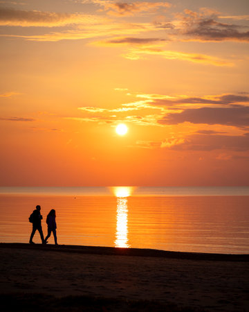 A beautiful summer sunset scenery with people silhouettes walking on a beach, enjoying Baltic Sea costline. Evening landscape of Latvia, Europe.の写真素材
