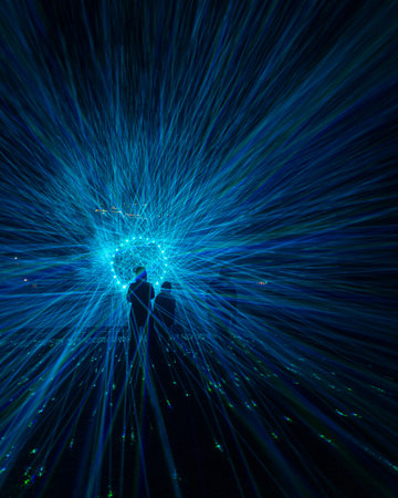 A group of people silhouettes agains a big light circle made of lasers. An art installation outdoors in Geiranger during Light Art Festival in winter, UNESCO World heritage area.
