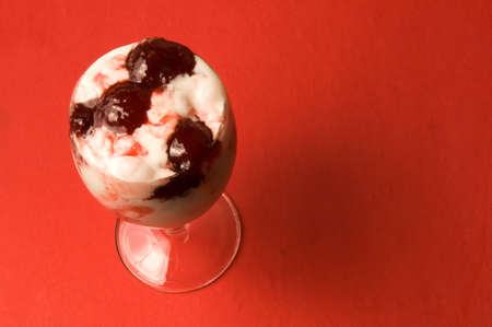 The glass with ice-cream with strawberry jam over red backgroundの写真素材