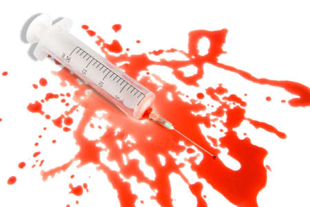 Medical syringe in the spatter blood puddle over white background. Small blood drop on the needle...
