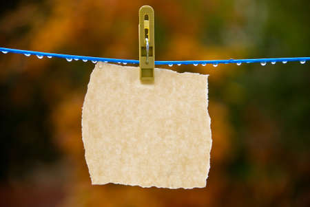 The torn off sheet of  paper hangs on a clothespin on a blue wire. There are water-drops on the wire. You can write  your message on the  paper.の写真素材