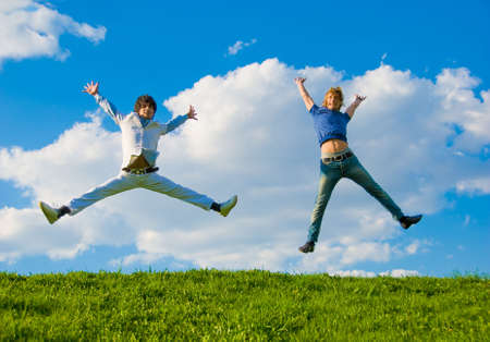 Happy teenagers jumping over green grass field. の写真素材