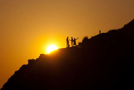 People silhouettes on a mountainside over sunsetの写真素材