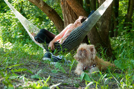 Woman relaxing in the hammock in a wood. Dog guards her dream. Focus to dog.の写真素材