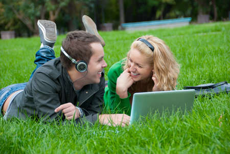 Young couple relax and listen to music from laptop on the grass in the parkの写真素材