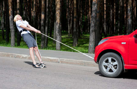 Blonde girl pulls a broken car with a ropeの写真素材