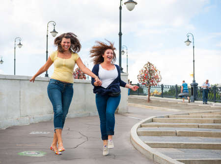 Two happy young beautiful women running on the streetの写真素材