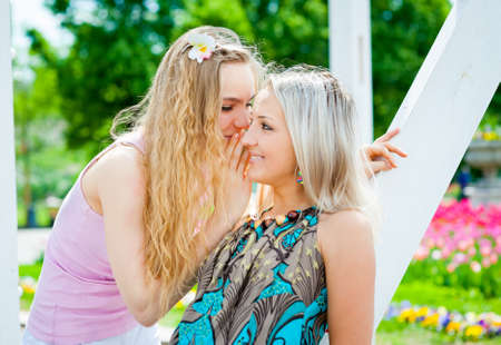 Two young women whispering outdoorsの写真素材