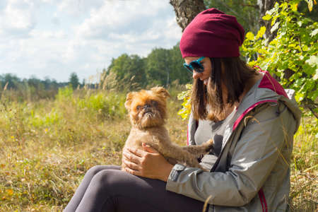 Young woman plays with small dog Griffon Bruxellois breed outdoorsの写真素材