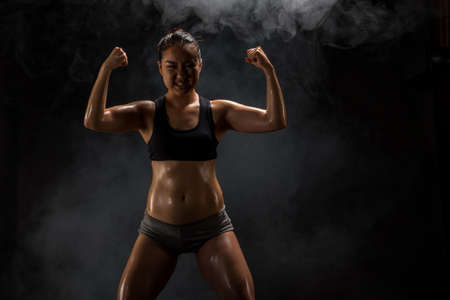 Young muscular asian woman posing on black backgroundの写真素材