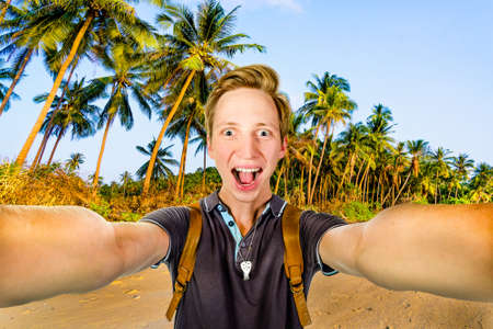 Young happy man taking selfie using front camera on a tropical beachの写真素材