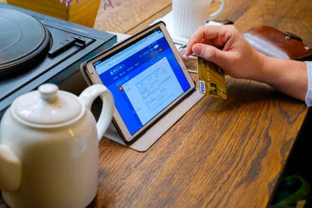 Moscow, Russia - September 10, 2016: Man searching for a trip on popular travel booking site using tablet pc in cafe at day time. He holds payment card in his handのeditorial素材