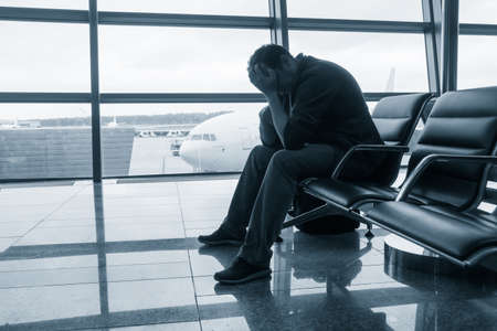 Sad man waiting for delayed flight in airportの写真素材