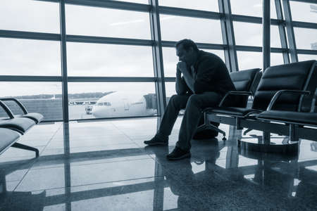Sad man waiting for delayed flight in airportの写真素材