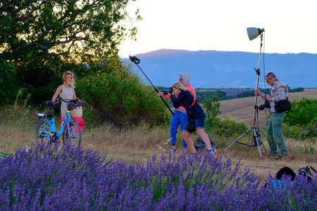 Valensole, France - July 6. 2016: Photographer and lighting assistant taking pictures of a young woman with a bicycle at sunrise at the rural road near lavender fieldのeditorial素材